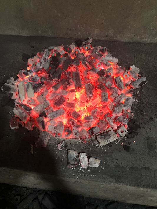 Traditional charcoal roasting workshop with rows of glowing charcoal pits and ash-covered hearths
